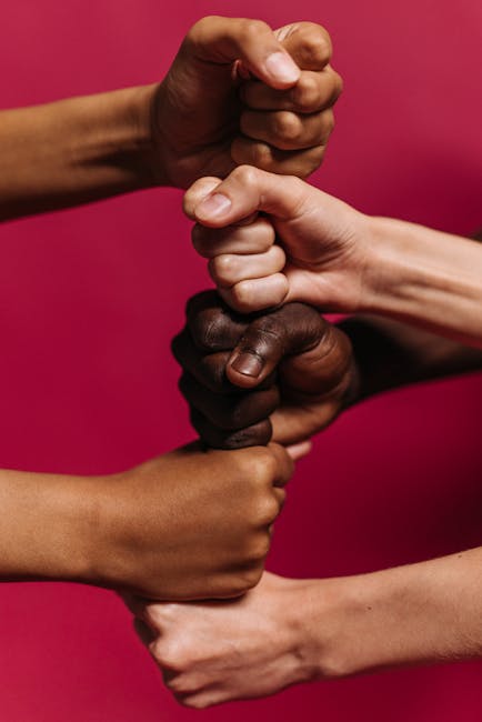 Close-up of diverse hands clenched together against a vibrant pink background symbolizing unity and strength.